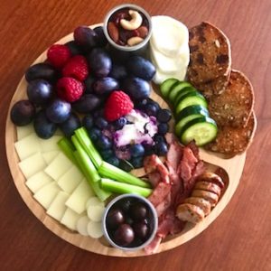 charcuterie board with fruit, vegetables, crackers, and trail mix