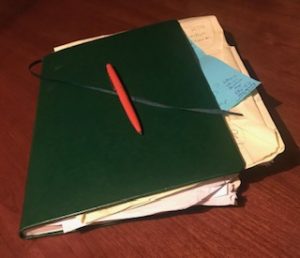 green planner that's stuffed with papers and an orange pen on top