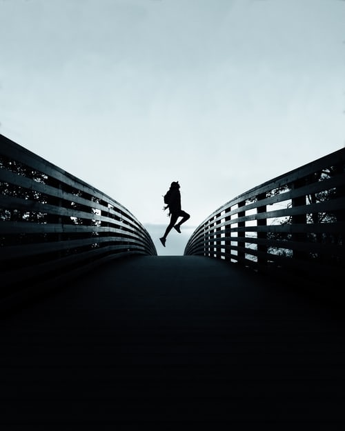 person jumping up while crossing a bridge